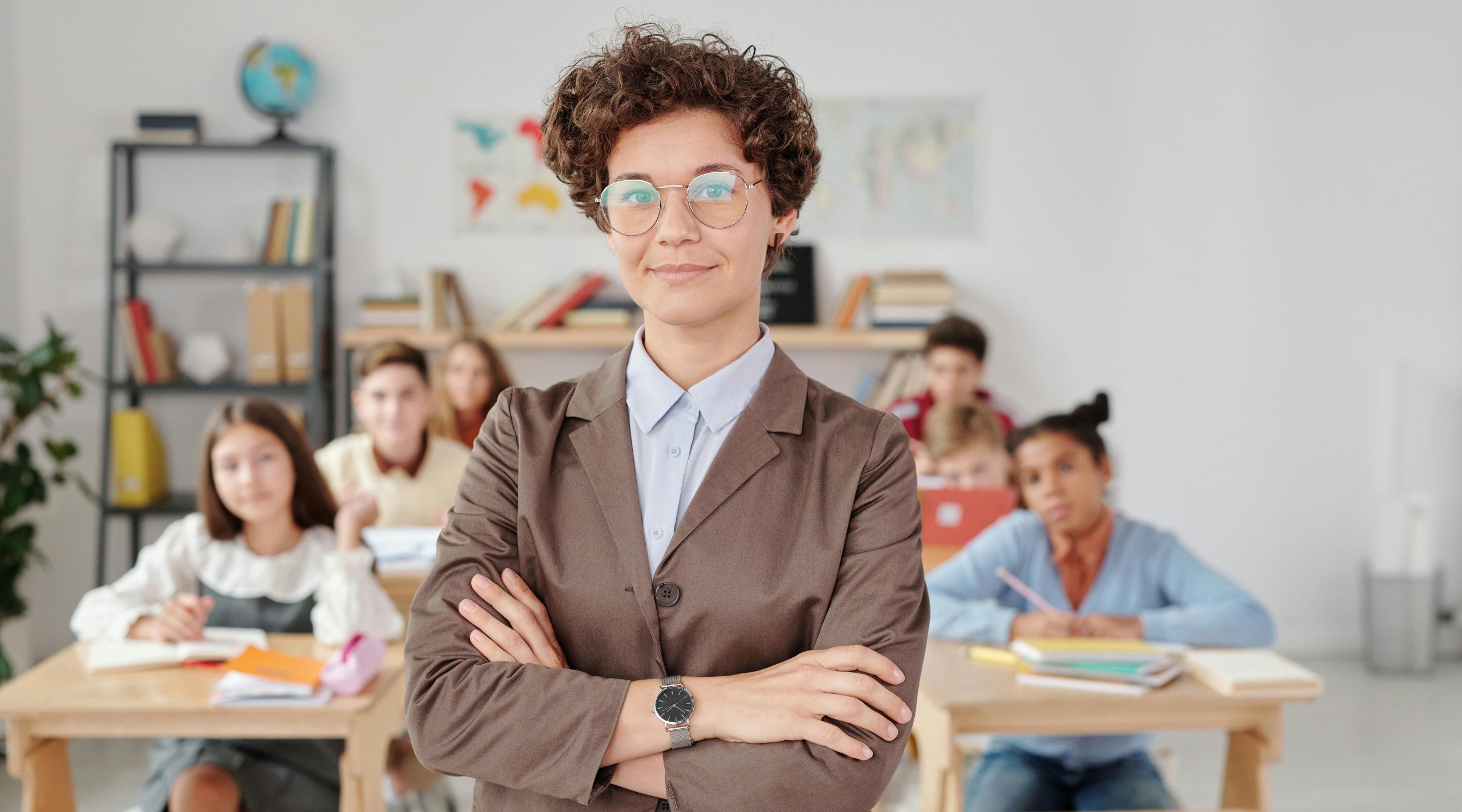 A confident teacher stands in front of students in a classroom setting.