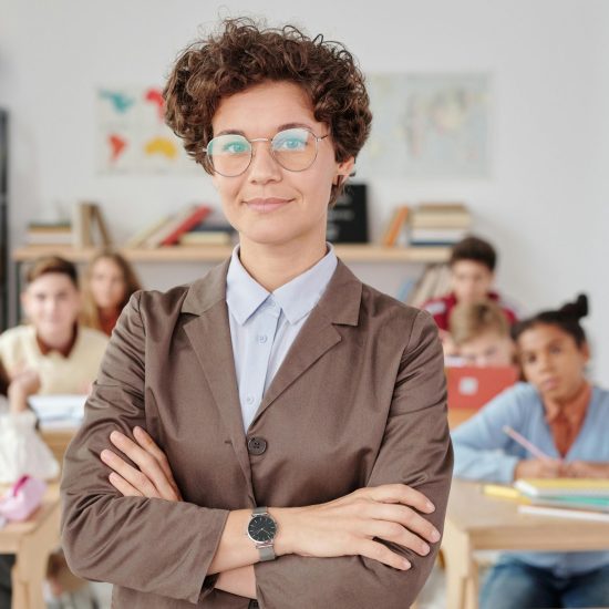 A confident teacher stands in front of students in a classroom setting.